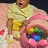 Milla is registered to the contest to win money with this photo: baby, child, yellow_clothing, headband, pink_blanket, plush_basket, easter_eggs, toy, indoor, happy, smiling, sock, face, person, cute, holiday, celebration, soft_texture, colorful, sitting