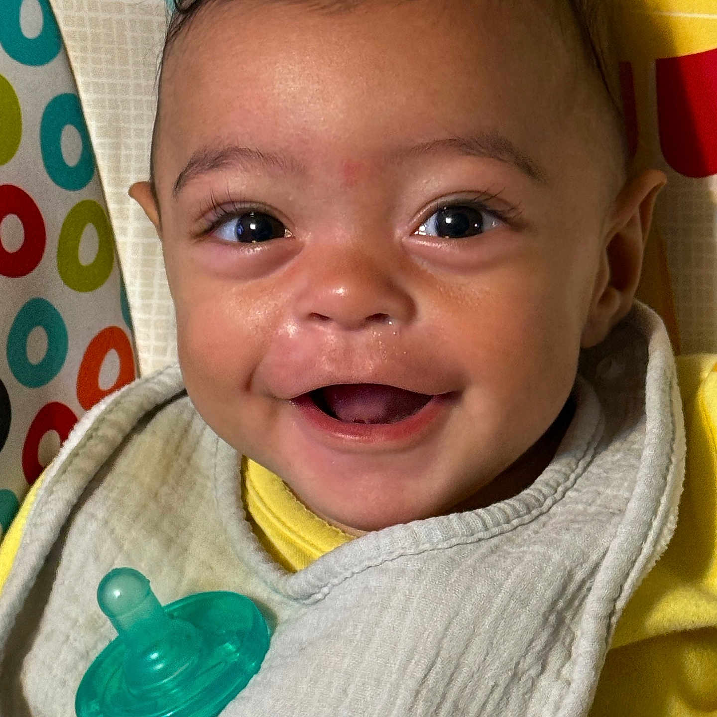 Milla joined the competition — help win amazing prizes! baby, smile, face, pacifier, bib, yellow_clothing, closeup, child, happy, infant, cheerful, cute, portrait, indoors, patterned_background, colorful, human, young_child, expression, eyelashes