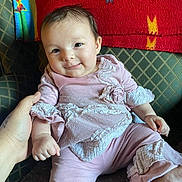 Lillian is registered to the contest to win money with this photo: baby, infant, smile, pink_clothing, hand, couch, blanket, face, person, cute, indoors, child, sitting, happy, furniture, portrait, soft_texture, home, young, cozy