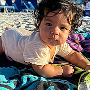 Javier joined the competition — help win amazing prizes! baby, child, curly_hair, towel, beach, sand, sunlight, outdoor, blue_sky, building, person, portrait, clothing, infant, relaxing, daytime, cute, closeup, summer, vacation