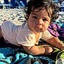 baby, child, curly_hair, towel, beach, sand, sunlight, outdoor, blue_sky, building, person, portrait, clothing, infant, relaxing, daytime, cute, closeup, summer, vacation