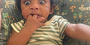 Mecca is registered to the contest to win money with this photo: baby, child, infant, face, hand, couch, cushion, striped_clothing, pacifier, indoor, surprised_expression, person, furniture, animal_pattern, seated, young_child, curly_hair, skin, arm, home