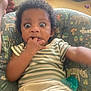 baby, child, infant, face, hand, couch, cushion, striped_clothing, pacifier, indoor, surprised_expression, person, furniture, animal_pattern, seated, young_child, curly_hair, skin, arm, home