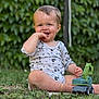 baby, background, child, cute, daylight, excavator, grass, greenery, hand_in_mouth, happy, mickey_mouse, nature, onesie, outdoor, playing, sitting, smiling, toddler, toy, young_child