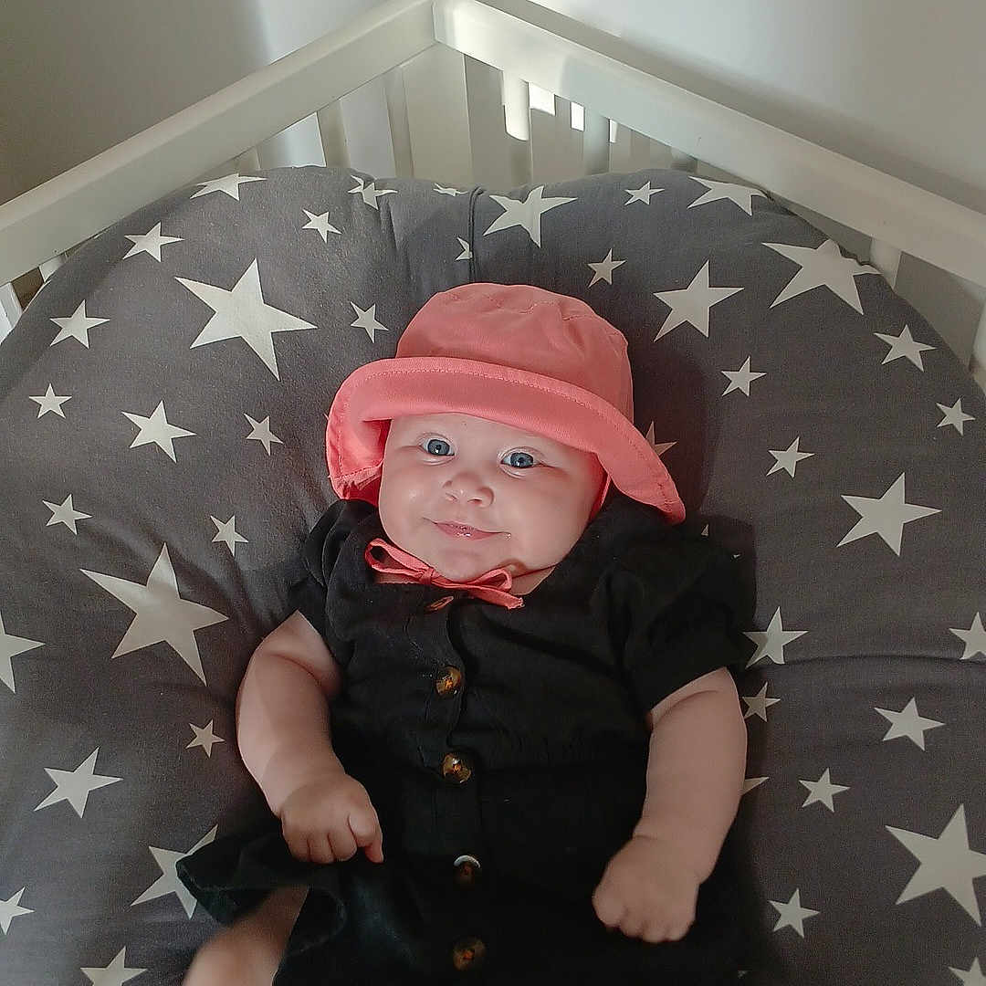Alizéa a rejoint le concours — aidez-le/la à gagner de superbes lots ! baby, black_dress, child, clothing, crib, cushion, cute, face, furniture, happy, hat, indoor, infant, light, person, plush, shadow, sitting, smile, stars
