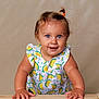 baby, blue_eyes, child, curious, cute, dress, hair_tie, hands, happy, indoor, lemon_pattern, light_background, person, portrait, smiling, standing, studio, toddler, wooden_surface, young_child