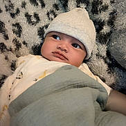 Aylann participe au concours pour gagner de l'argent avec cette photo : baby, infant, hat, blanket, cozy, face, expression, curious, lying_down, soft_texture, patterned_background, clothing, child, cute, portrait, indoors, resting, newborn, warm, snug