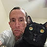 Oliver Wendle is registered to the contest to win money with this photo: adult, animal, black_cat, cat, ceiling_fan, close_up, expression, eyes, face, feline, fur, home, indoor, man, person, pet, portrait, reflection, selfie, white_shirt
