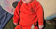 Liam joined the competition — help win amazing prizes! baby, infant, orange_clothing, plush_pillow, tie_dye, stuffed_animal, blue_eyes, sitting, indoors, soft_toy, cute, child, portrait, cozy, fabric, relaxed, small_hands, bare_feet, colorful, expression