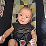 Liam joined the competition — help win amazing prizes! baby, infant, car_seat, safety_harness, child, cute, wide_eyes, expression, patterned_background, black_clothing, seat_belt, indoor, portrait, young_child, seated, looking_up, skin, person, baby_boy, closeup