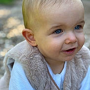 Romy a rejoint le concours — aidez-le/la à gagner de superbes lots ! toddler, child, face, blue_eyes, fur_vest, white_clothing, outdoor, portrait, curious, smile, baby, cute, soft_texture, blurred_background, skin, head, person, young_child, looking_away, close_up