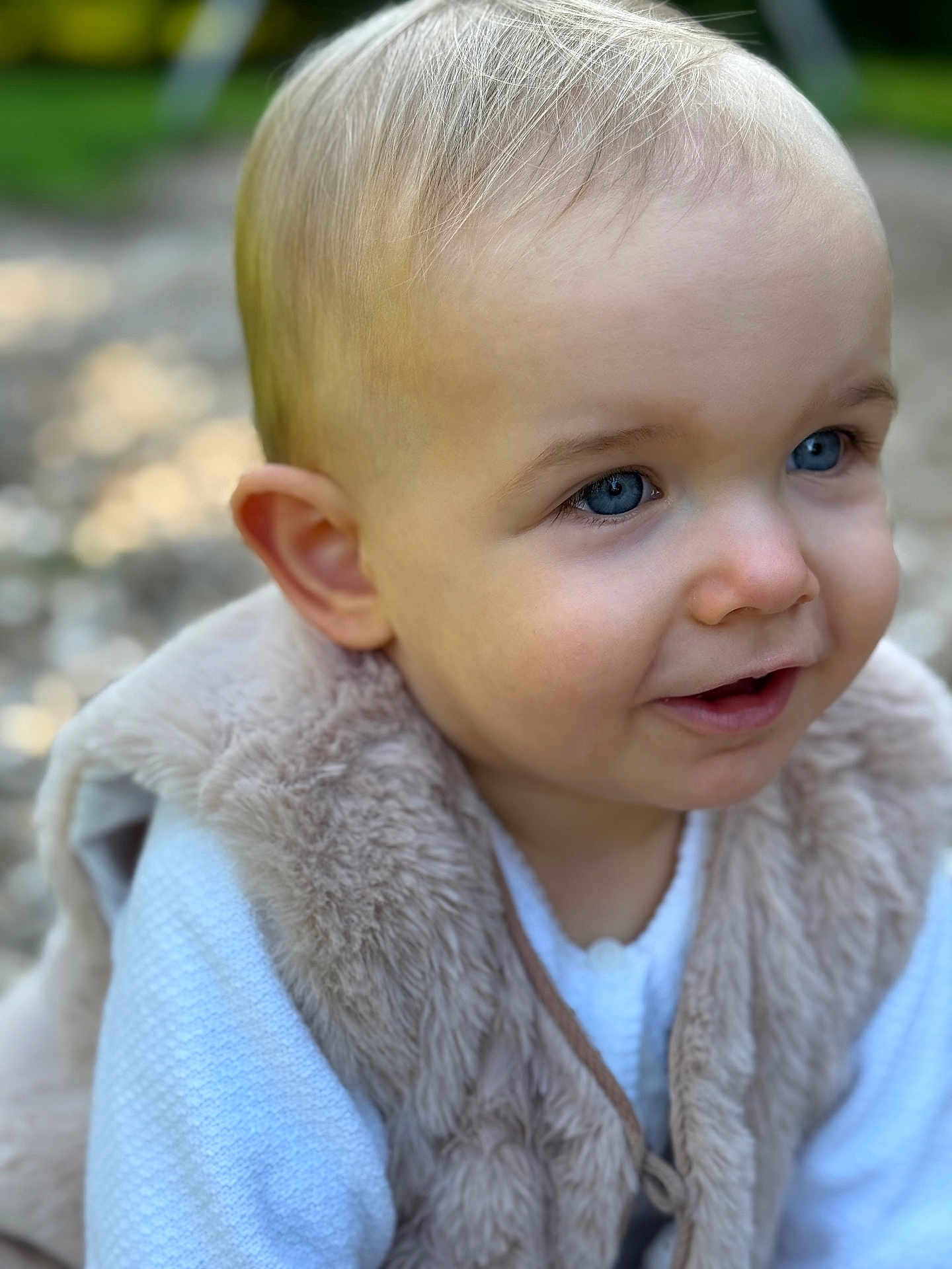 Romy a rejoint le concours — aidez-le/la à gagner de superbes lots ! toddler, child, face, blue_eyes, fur_vest, white_clothing, outdoor, portrait, curious, smile, baby, cute, soft_texture, blurred_background, skin, head, person, young_child, looking_away, close_up