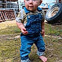 toddler, child, barefoot, denim_overalls, outdoor, rustic, tires, grass, moss, curious, young_child, blue_eyes, short_hair, casual_clothing, nature, daylight, standing, person, cute, expression