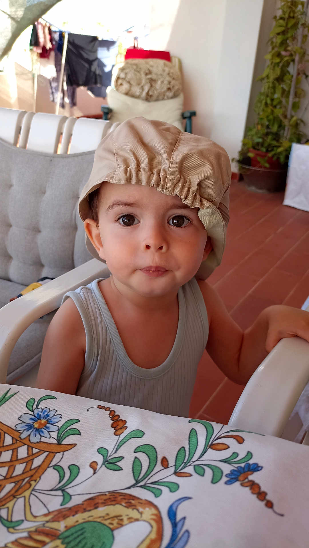 Joachim a rejoint le concours — aidez-le/la à gagner de superbes lots ! toddler, child, hat, table, tablecloth, floral_pattern, indoor, curious, face, eyes, arm, chair, furniture, casual_clothing, expression, person, seated, home, daylight, plant