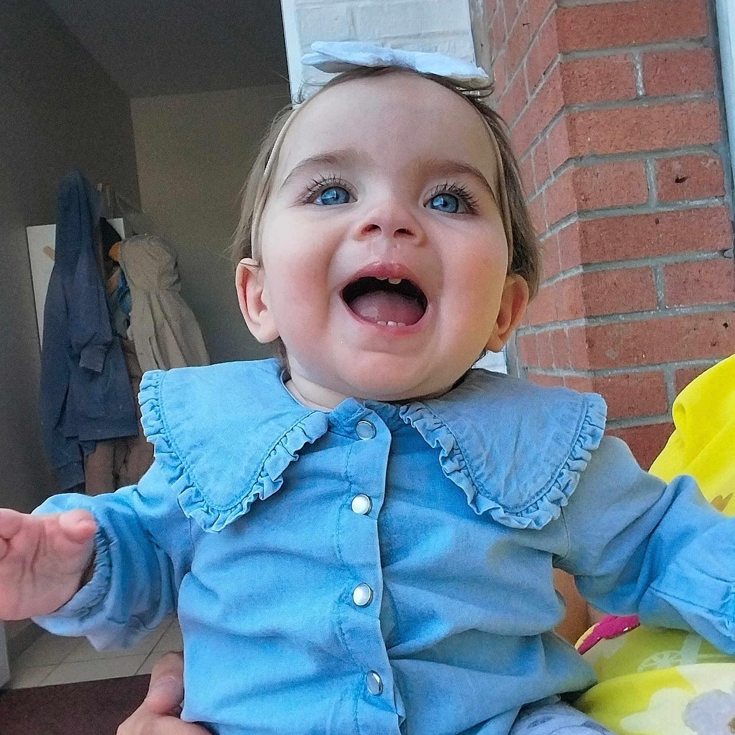 Louméa participe au concours pour gagner de l'argent avec cette photo : baby, blue_eyes, blue_shirt, bow, brick_wall, candid, child, clothing, coat, doorway, face, hand, happy, headband, holding, indoor, person, portrait, smiling, toddler