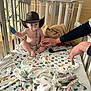 Madelyn joined the competition — help win amazing prizes! baby, cowboy_hat, pacifier, crib, hospital, blanket, remote_control, hand, adult, wristband, child, sitting, diaper, bed, person, colorful, patterned, indoor, furniture, cute