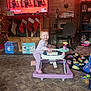 Madelyn is registered to the contest to win money with this photo: toddler, walker, carpet, living_room, christmas_stockings, christmas_lights, television, musical_performance, toys, child, smiling, purple, furniture, desk, chair, bookshelf, holiday_decor, blanket, plush_toy, home
