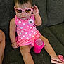 baby, child, sunglasses, pink, polka_dot, dress, sippy_cup, couch, footwear, flip_flops, indoor, cute, portrait, sitting, person, infant, fashion, accessory, relaxing, home
