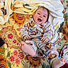 River is registered to the contest to win money with this photo: baby, child, smiling, onesie, blanket, floral_pattern, indoor, happy, feet, clothing, fabric, cute, infant, playful, person, portrait, bedspread, colorful, sitting, cozy