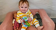 River joined the competition — help win amazing prizes! toddler, child, pajamas, yellow_stripes, pink_chair, book, doll, plush_toy, smiling, indoor, flooring, wood_floor, cute, happy, seated, playing, toy, person, baby, portrait