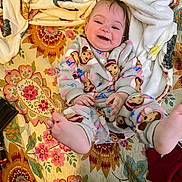 River joined the competition — help win amazing prizes! baby, child, smiling, onesie, monkey_pattern, blanket, floral_pattern, feet, happy, indoors, couch, fabric, toddler, cozy, playful, cute, infant, person, colorful, portrait