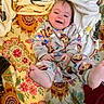 baby, child, smiling, onesie, monkey_pattern, blanket, floral_pattern, feet, happy, indoors, couch, fabric, toddler, cozy, playful, cute, infant, person, colorful, portrait