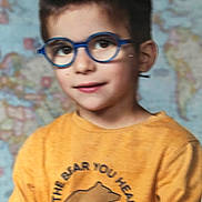 Gabriel a rejoint le concours — aidez-le/la à gagner de superbes lots ! child, boy, glasses, yellow_shirt, bear_graphic, map_background, portrait, smiling, short_hair, indoors, casual_clothing, cute, young, face, eyewear, person, head, happy, kid, people