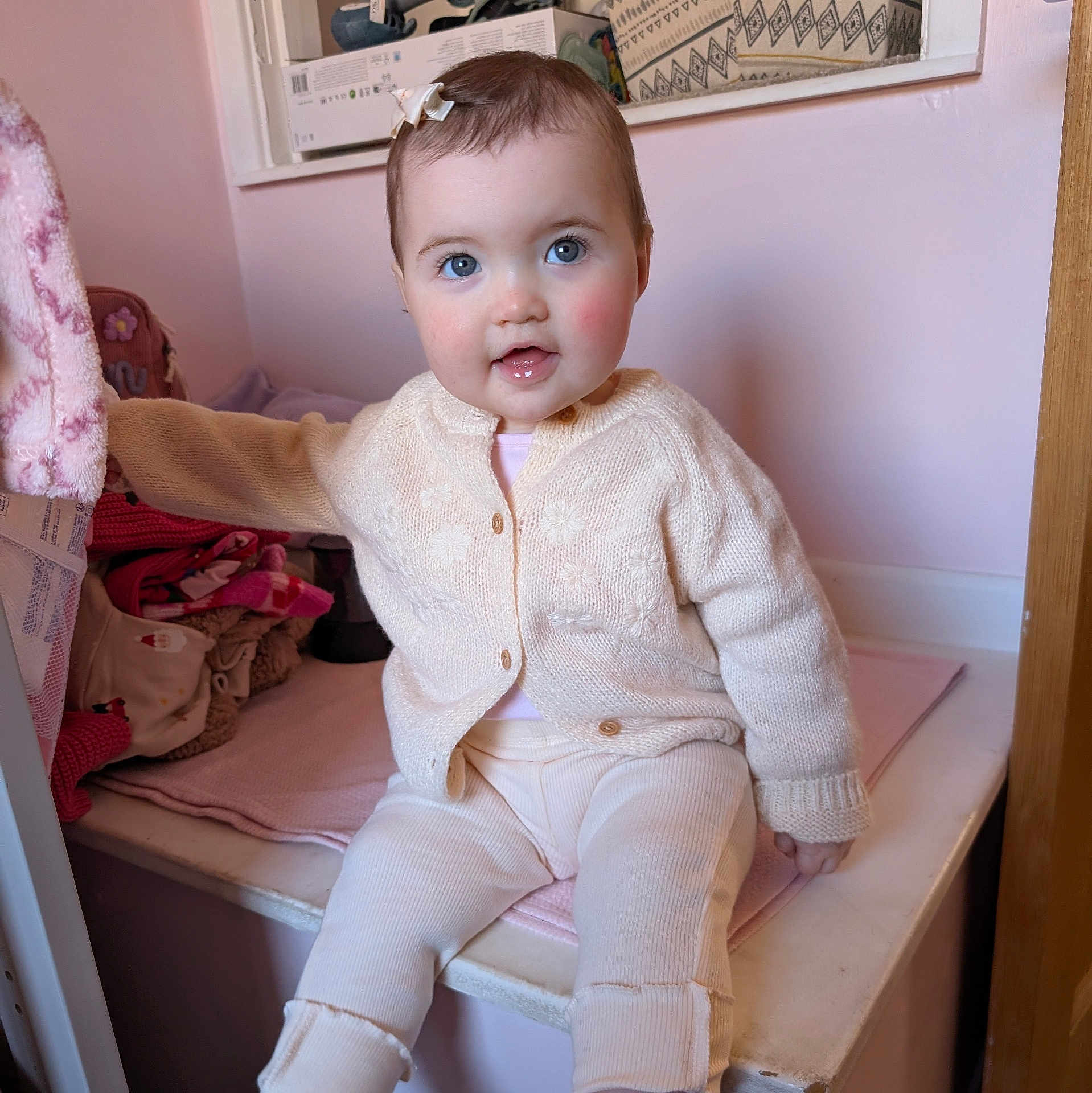 Bowen Belle is registered to the contest to win money with this photo: baby, child, infant, blue_eyes, rosy_cheeks, cream_sweater, knitwear, pants, indoor, cozy, soft_texture, pink, fabric, cute, smiling, seated, person, portrait, young_child, playful