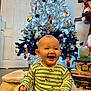 baby, celebration, child, christmas_lights, christmas_tree, decorations, face, festive, floor, gift_boxes, happy, holiday, indoor, ornaments, pajamas, person, sitting, smiling, striped_clothing, toy