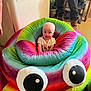 baby, infant, bean_bag, colorful, rainbow, poop_emoji, indoor, person, smiling, plush, furniture, child, cute, seat, toy, soft, candid, happy, home, googly_eyes