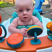 Malachi is registered to the contest to win money with this photo: baby, infant, child, activity_center, toy, outdoor, backyard, inflatable_shark, blue_eyes, curious, summer, person, seat, hands, plastic_toy, playtime, fence, adult, footwear, concrete