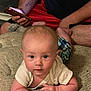 Malachi joined the competition — help win amazing prizes! baby, infant, child, person, blanket, tattoo, phone, hand, face, arm, clothing, sitting, casual, indoor, adult, red_shorts, black_shirt, plaid_shorts, curious, texture