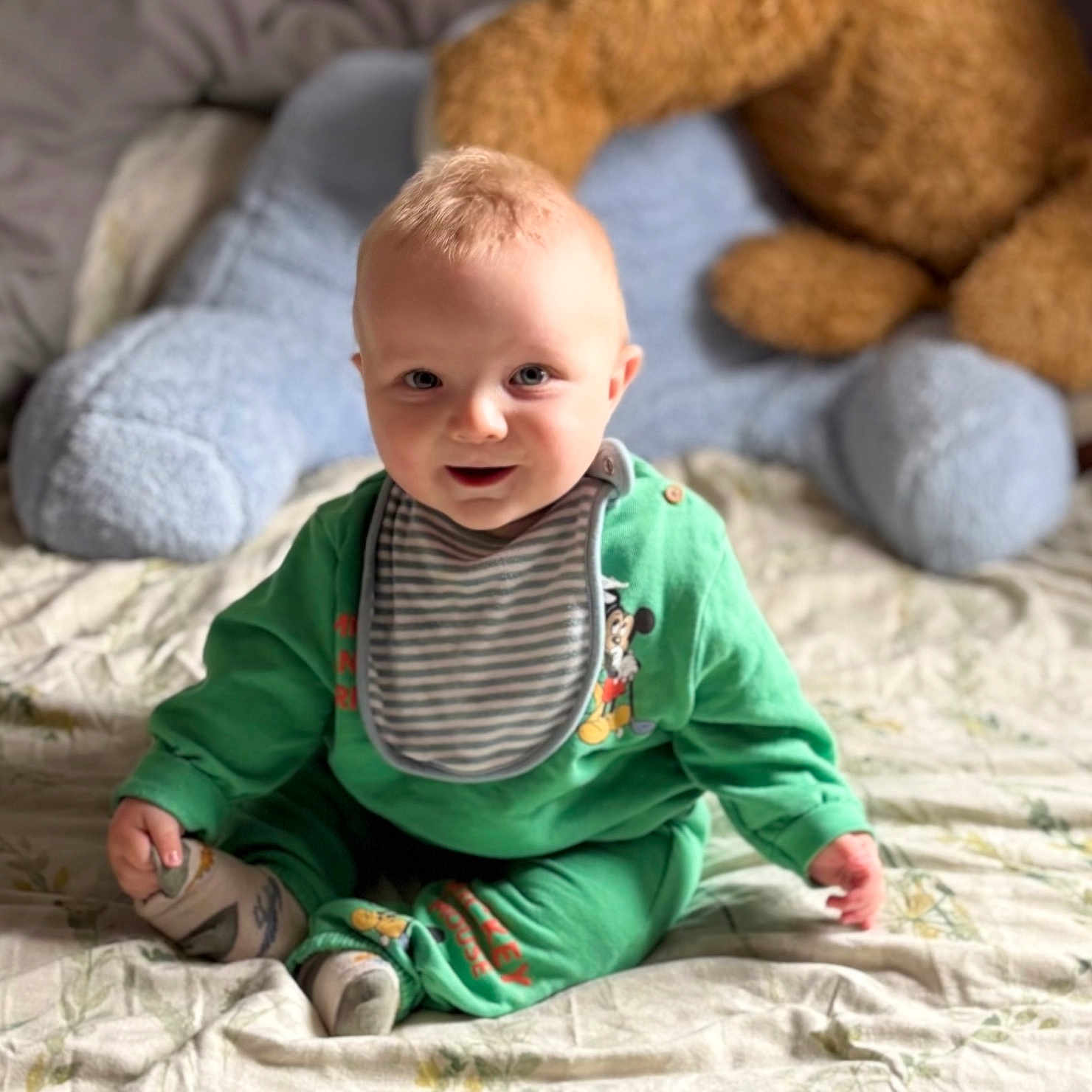 Ted joined the competition — help win amazing prizes! baby, bedspread, child, childrens_room, cozy, curious, cute, footwear, green_clothing, happy, indoor, infant, playful, plush_toy, portrait, sitting, smiling, soft_toys, striped_bib, stuffed_animal