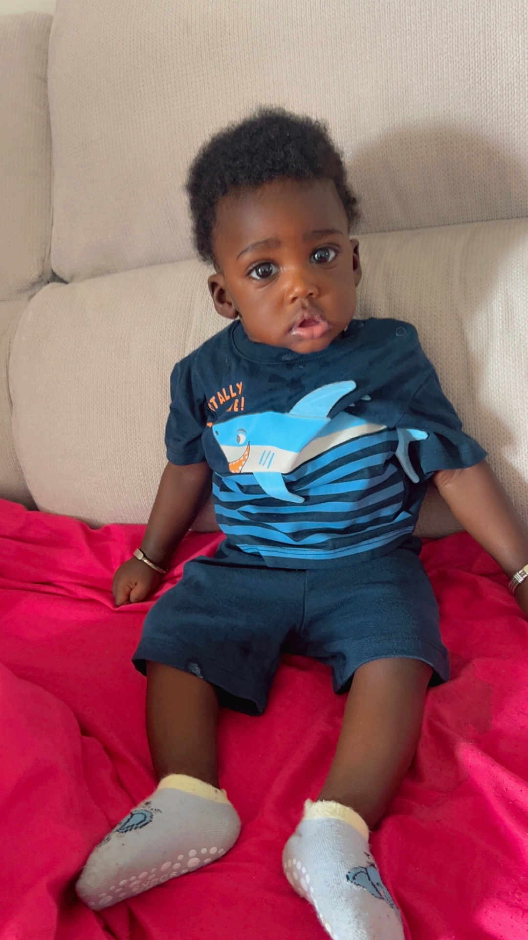 Iyad a rejoint le concours — aidez-le/la à gagner de superbes lots ! child, toddler, baby, sitting, sofa, blanket, clothing, shirt, shorts, socks, indoor, person, face, expression, curly_hair, bracelet, casual, home, comfort, cute