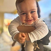 Loukas a rejoint le concours — aidez-le/la à gagner de superbes lots ! baby, infant, smiling, face, eyes, cheeks, hands, arms, onesie, clothing, close_up, portrait, indoor, bokeh, blurred_background, parent_holding, happiness, cute, soft_lighting, toddler