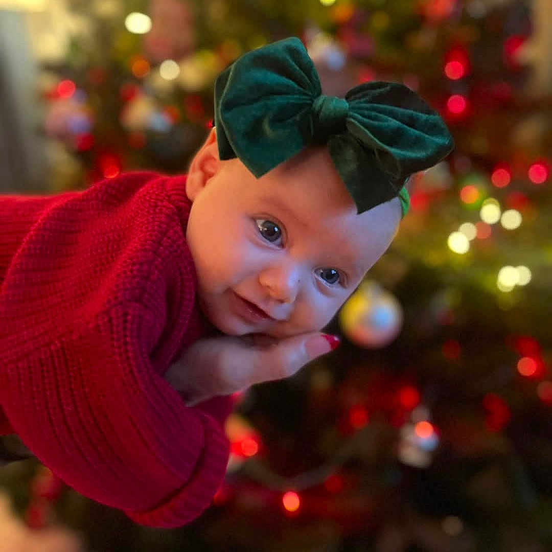 Kinsley is registered to the contest to win money with this photo: accessories, baby, christmas, christmasdecorations, christmastree, clothing, crawling, face, festival, hair, happy, head, knitwear, person, photography, portrait, scarf, sleeve, smile, sweater