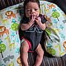 Cayden is registered to the contest to win money with this photo: animal_print, baby, black_onesie, child, colorful, curly_hair, cute, fingers_in_mouth, giraffe, hippopotamus, indoors, infant, leather_chair, lion, owl, pillow, portrait, relaxed, seated, small_feet