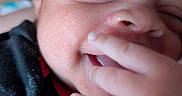 Cayden joined the competition — help win amazing prizes! baby, close_up, smile, face, fingers, black_clothing, infant, skin, happy, portrait, cute, child, young, expression, person, hand, sleepy, indoors, soft_light, blurry_background