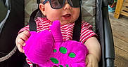 David joined the competition — help win amazing prizes! baby, sunglasses, plush_toy, stroller, child, smiling, red_striped_clothing, seat_belt, indoor, wooden_floor, happy, person, toy, fun, cute, infant, casual, comfort, playful, relaxed