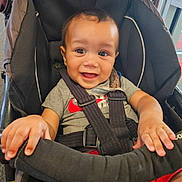 Mateo is registered to the contest to win money with this photo: baby, black, car_seat, child, clothing, cute, eyes, fabric, face, gray_shirt, hair, happy, indoors, red_shorts, safety_harness, seat, short_sleeve, small_hands, smiling, toddler