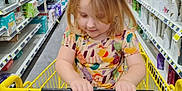Hailey joined the competition — help win amazing prizes! toddler, child, shopping_cart, store_aisle, colorful_clothing, blonde_hair, holding, handlebar, sitting, grocery_store, products, shelves, floor, casual, indoor, shopping, young_child, retail, curly_hair, happy