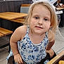 child, bunny_ears, blue_dress, floral_pattern, restaurant, tray, chicken_nuggets, table, chair, face, smudges, blonde_hair, curious_expression, indoor, food, person, seat, casual, messy_face, young