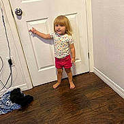 Hailey joined the competition — help win amazing prizes! toddler, child, barefoot, standing, pointing, shorts, shirt, heart_pattern, door, wooden_floor, indoor, wall, curious, young_child, person, clothing, hair, room, floor, expression
