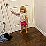 toddler, child, barefoot, standing, pointing, shorts, shirt, heart_pattern, door, wooden_floor, indoor, wall, curious, young_child, person, clothing, hair, room, floor, expression