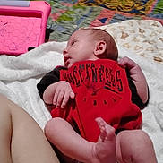 Makenzie is registered to the contest to win money with this photo: baby, infant, blanket, red_clothing, tampa_bay_buccaneers, tablet_case, colorful_quilt, leg, indoors, person, skin, hand, foot, lying_down, bedroom, soft_texture, patterned_fabric, comfort, casual, resting
