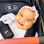 baby, infant, smile, headband, heart_headband, stroller, seat_harness, handlebar, blanket, white_clothing, chubby_cheeks, bright_eyes, closeup, portrait, happy, accessory, soft_lighting, bokeh, textile, pram