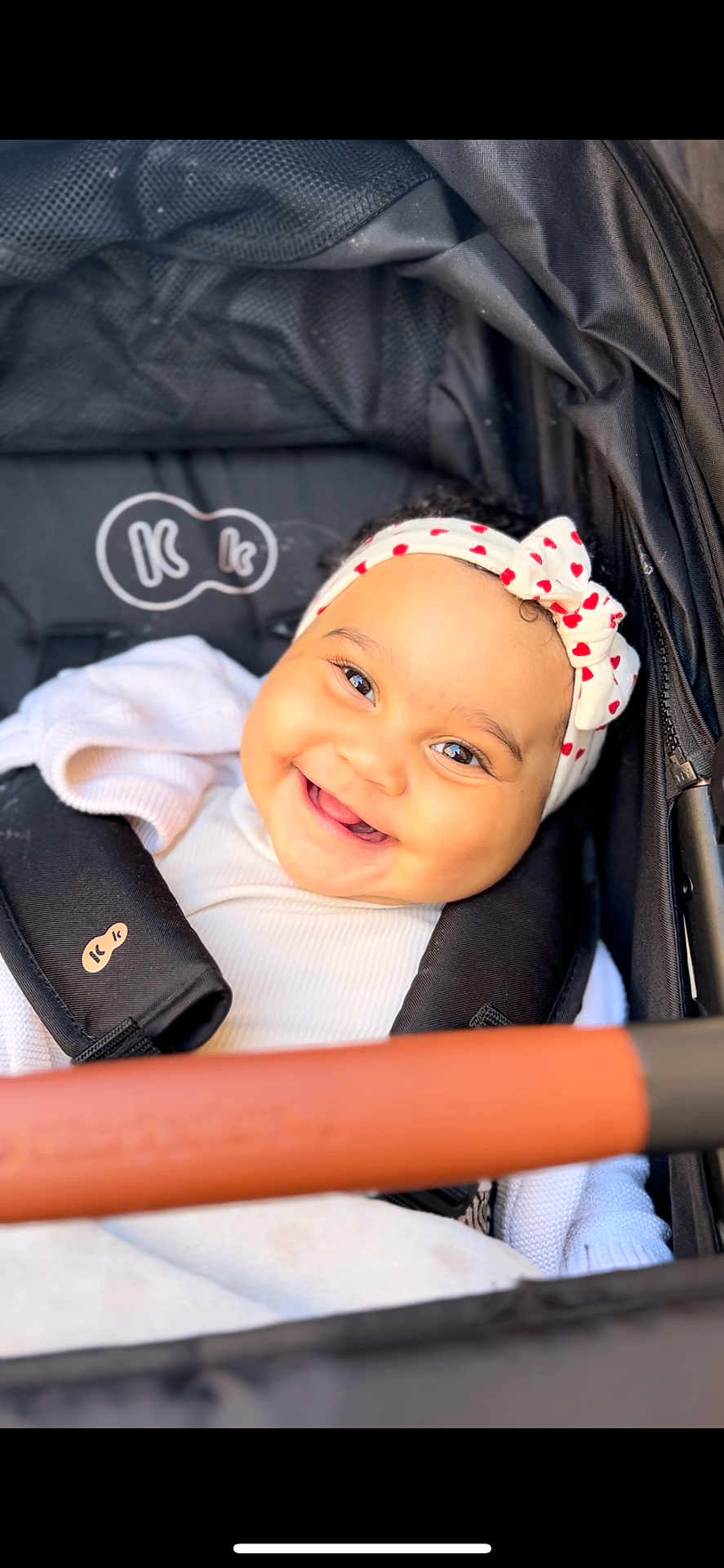 Keyla participe au concours pour gagner de l'argent avec cette photo : baby, infant, smile, headband, heart_headband, stroller, seat_harness, handlebar, blanket, white_clothing, chubby_cheeks, bright_eyes, closeup, portrait, happy, accessory, soft_lighting, bokeh, textile, pram