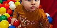 Margo is registered to the contest to win money with this photo: baby, child, toddler, play_area, ball_pit, colorful_balls, headband, bow, orange_clothing, white_tights, indoor, cute, portrait, seated, hands, expression, play, toy, soft_lighting, closeup