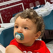 Ridha a rejoint le concours — aidez-le/la à gagner de superbes lots ! toddler, child, pacifier, red_shirt, curly_hair, indoor, dining_room, wine_glasses, table, chair, face, portrait, looking_away, young_child, person, casual_clothing, cute, baby, expression, seated