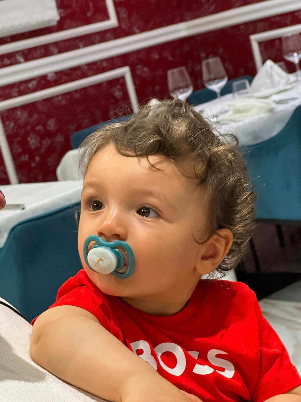 Ridha a rejoint le concours — aidez-le/la à gagner de superbes lots ! toddler, child, pacifier, red_shirt, curly_hair, indoor, dining_room, wine_glasses, table, chair, face, portrait, looking_away, young_child, person, casual_clothing, cute, baby, expression, seated